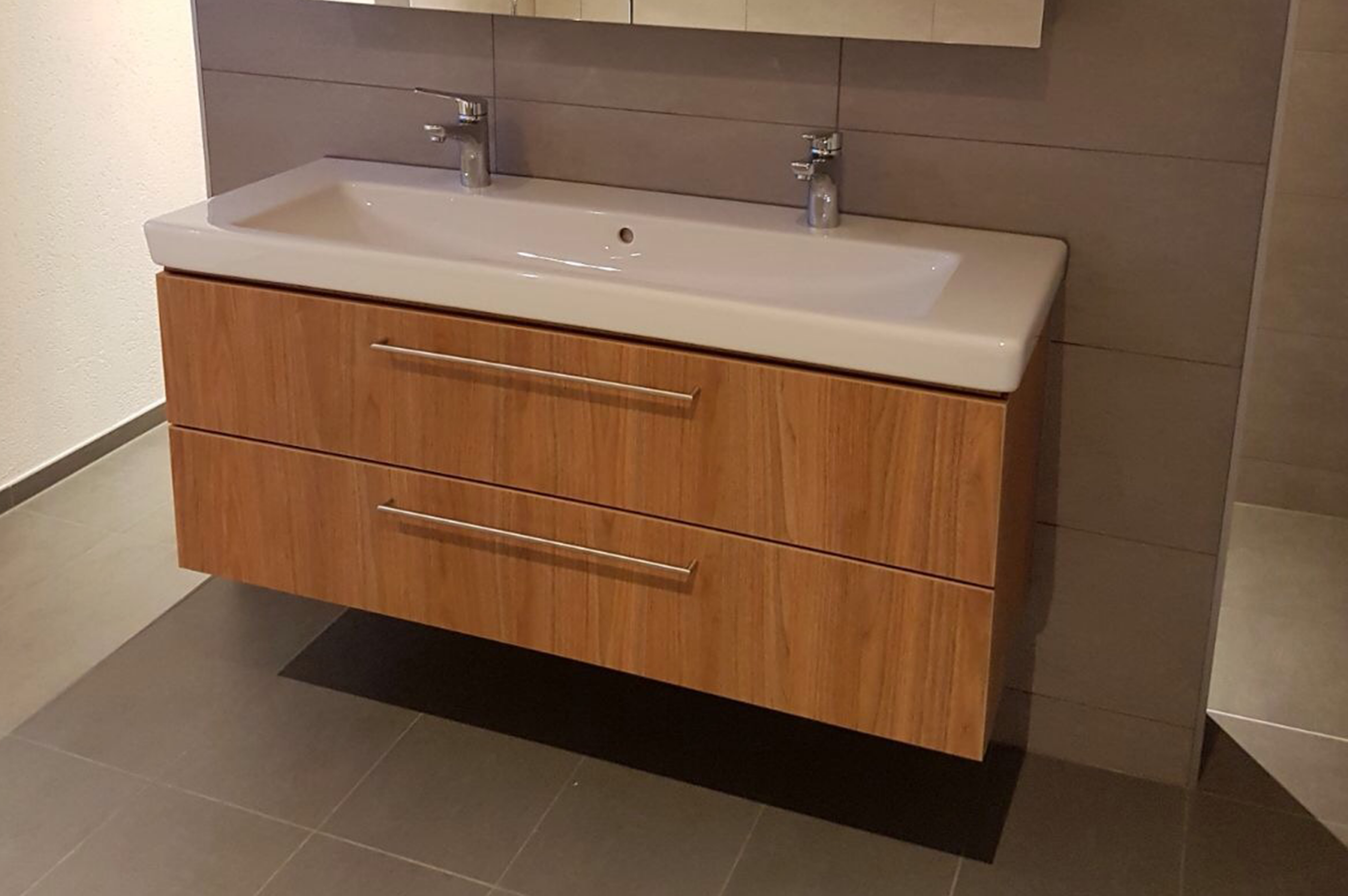 2 Moderner Waschtisch mit Holzunterschrank und Doppelarmaturen in stilvollem Badezimmer-Design.